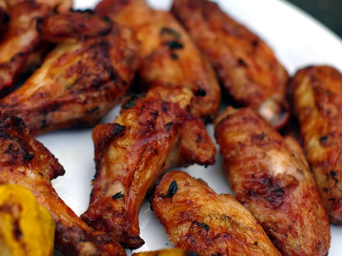 Close-up of glazed, charred grilled chicken wings sprinkled with herbs on a white plate