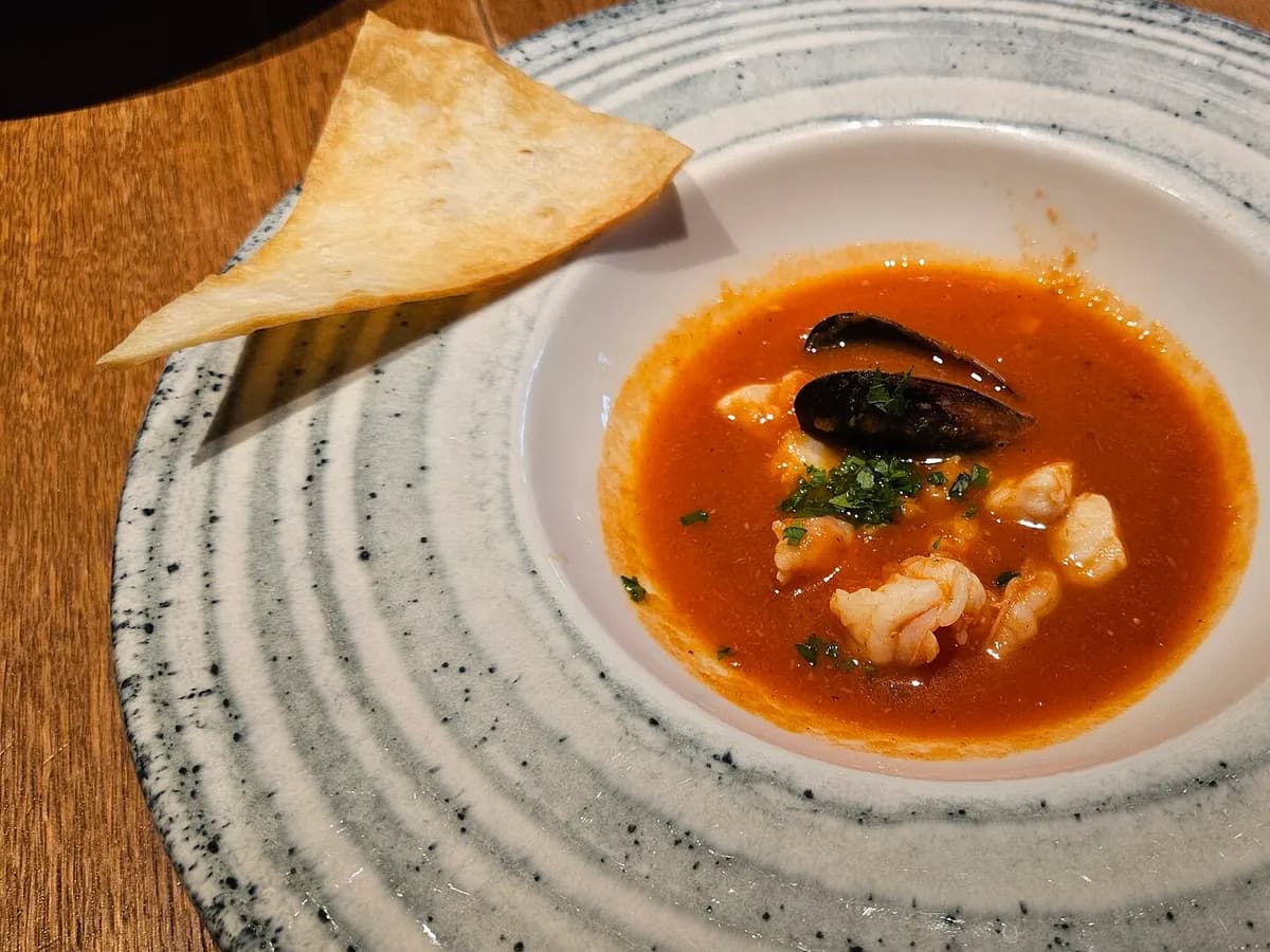 Bowl of rich tomato fish soup with prawns, a mussel and chopped parsley on a speckled ceramic plate